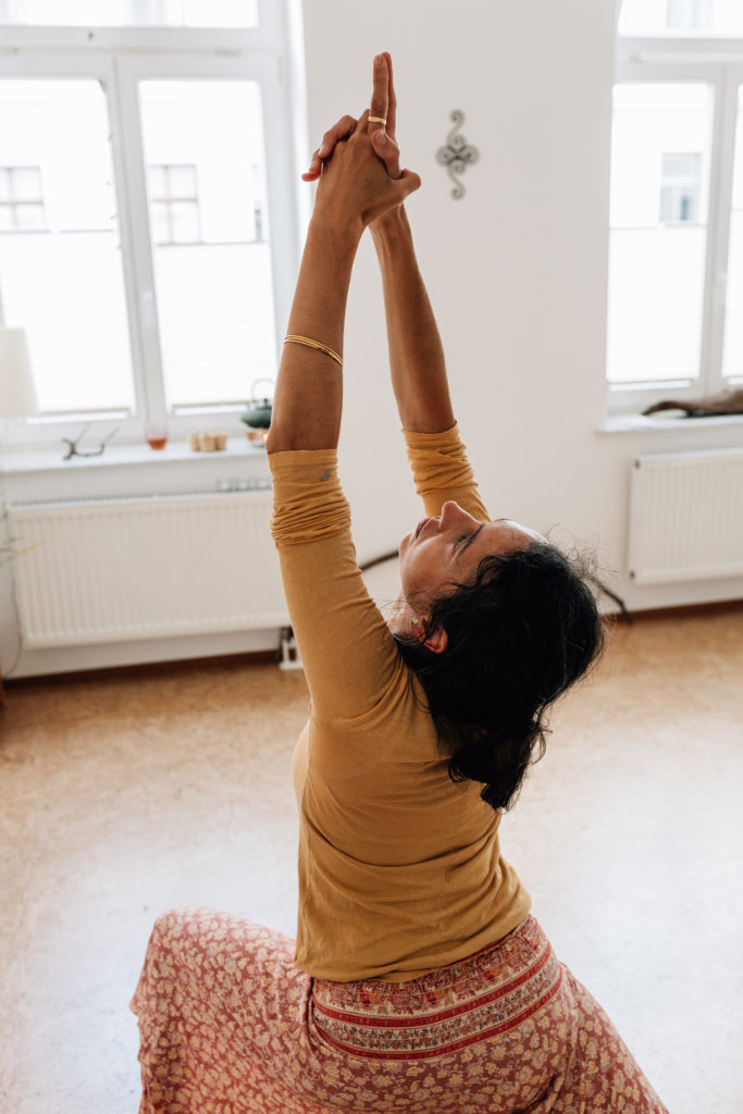 Die Yogalehrerin Maria Lichtenberg richtet in der Kriegervariante 1/ Vīrabhadrāsana 1 den Blick nach oben in ihre Handinnenflächen und hält dabei die Balance in ihrem Yogaraum in Leipzig.