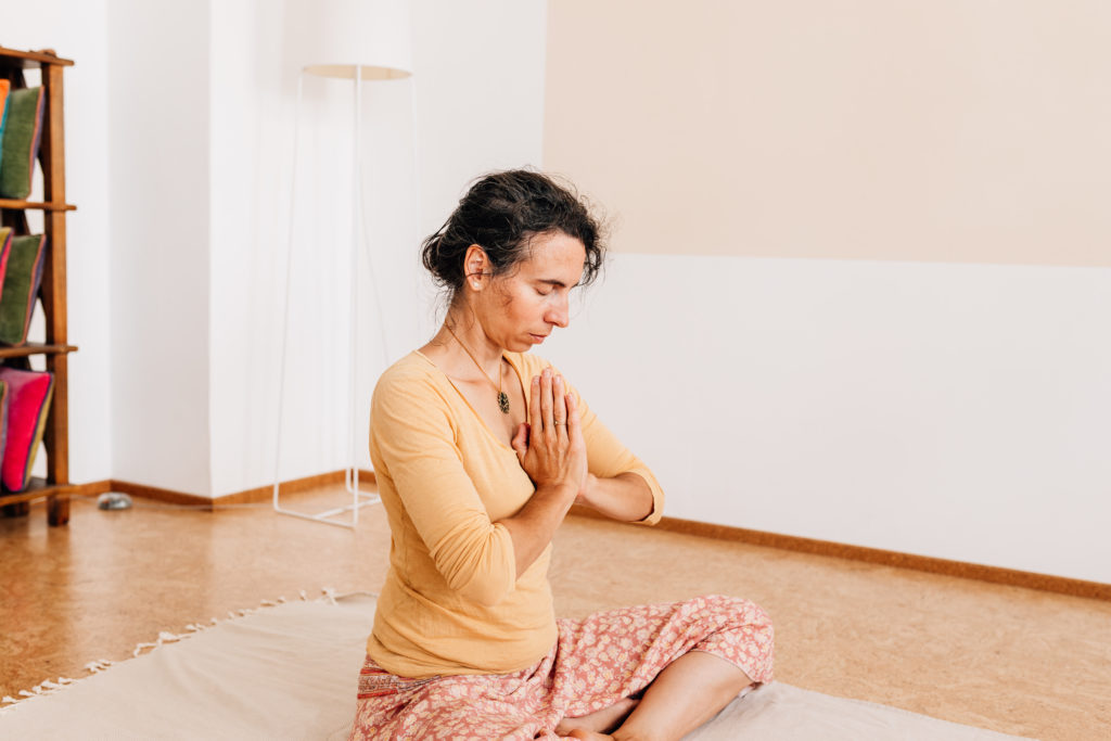 Die Yogalehrerin Maria Lichtenberg verneigt sich und hält ihre Hände vor dem Herzen in Anjali mudra in ihrem Yogaraum in Leipzig.