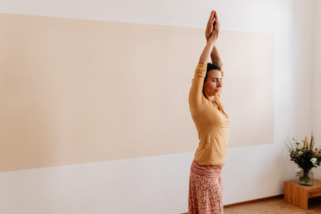 Die Yogalehrerin Maria Lichtenberg bringt im Sitzen ihre Fußsohlen zueinander, platziert die Hände auf den Fußrücken und neigt sich mit geradem Oberkörper nach vorn in ihrem Yogaraum in Leipzig.