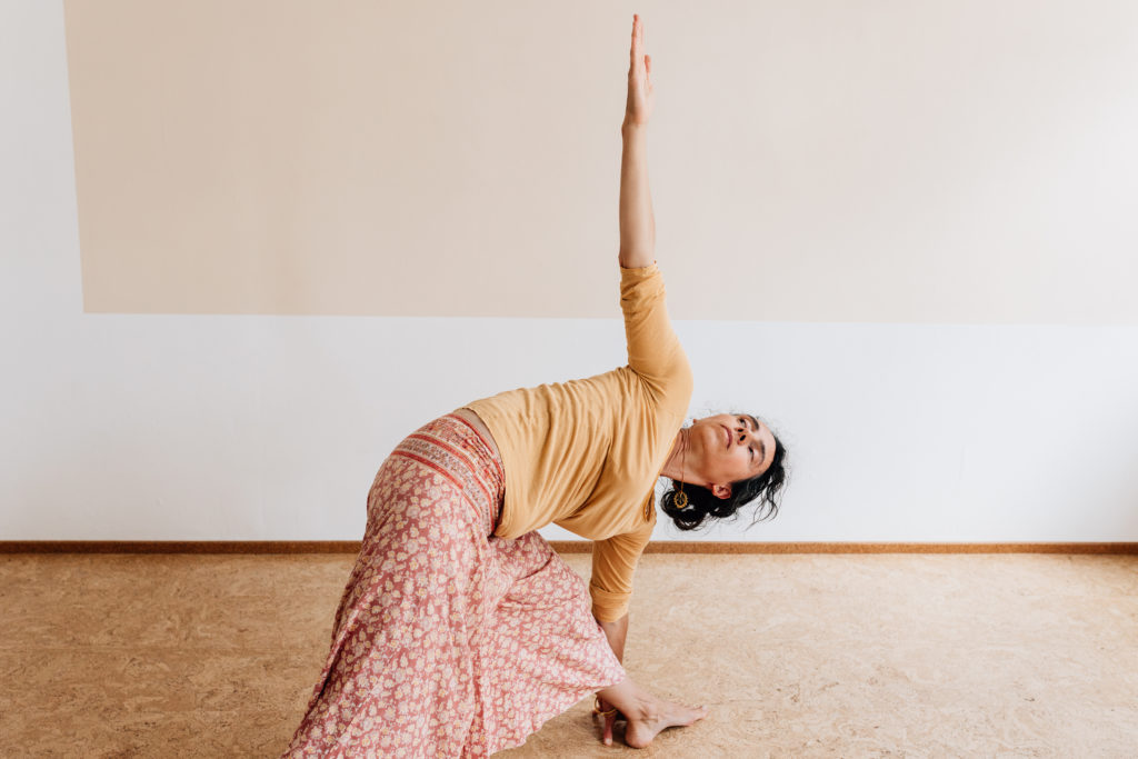 Die Yogalehrerin Maria Lichtenberg verweilt im ausgestreckten Dreieck/ utthita-trikonasana (von der Seite fotografiert) in ihrem Yogaraum in Leipzig.
