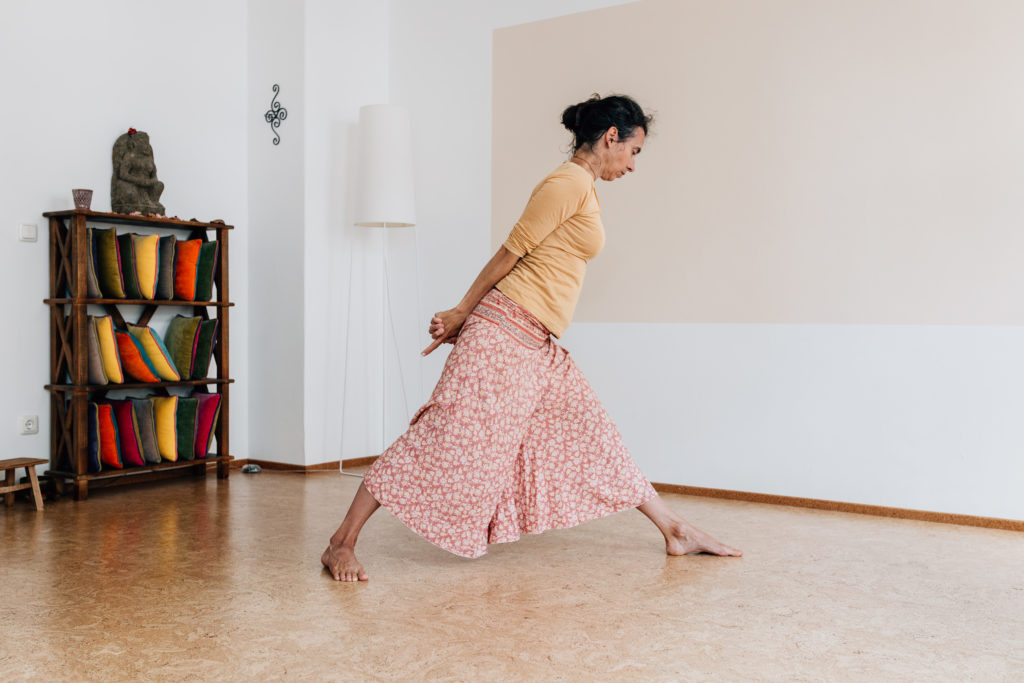 Die Yogalehrerin Maria Lichtenberg kommt mit geradem Rücken nach oben während die Hände hinter dem Rücken verschränkt sind und den Oberkörper beim Hochkommen stützen in ihrem Yogaraum in Leipzig.