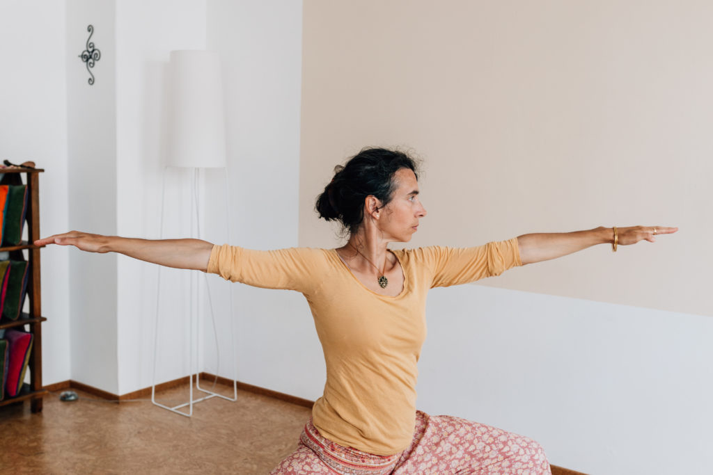 Die Yogalehrerin Maria Lichtenberg praktiziert die Kriegervariante 2/ Vīrabhadrāsana 2 und fokussiert ihr (nächstes) Ziel in ihrem Yogaraum in Leipzig.