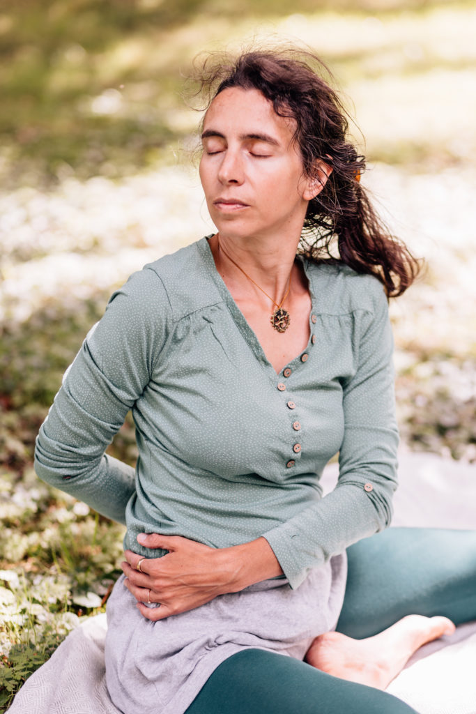 Die Yogalehrerin Maria Lichtenberg entspannt sich über tiefe vollständige Ausatmungen in der Drehhaltung, so dass diese fest/ stabil und gleichzeitig angenehm/ bequem ist in der freien Natur (in der Nähe ihres Yogaraumes in Leipzig).