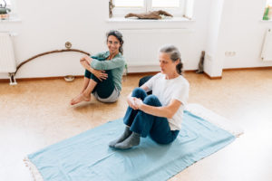 Die Yogalehrerin Maria Lichtenberg praktiziert mit einer Yogaschülerin das goldene Ei (Hiranya-garbhasana) - das Gesäß ist am Boden, die Arme umgreifen die Beine, die Füße sind in der Luft, der Rücken ist gerade und das Herz darf sich heben. Kopf- und Nackenbereich sind entspannt.