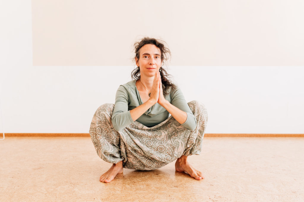 Die Yogalehrerin Maria Lichtenberg verweilt in einer tiefen Hocke und hat die Handinnenflächen zueinander geführt in ihrem Yogaraum in Leipzig.