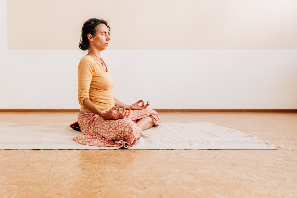 Die Yogalehrerin Maria Lichtenberg meditiert in einer aufrechten festen und gleichzeitig entspannten meditativen Sitzhaltung in ihrem Yogaraum in Leipzig.