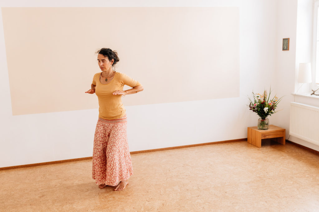 Die Yogalehrerin Maria Lichtenberg verwurzelt sich indem sie die Energie ausatmend mit den Armen nach unten lenkt in ihrem Yogaraum in Leipzig.