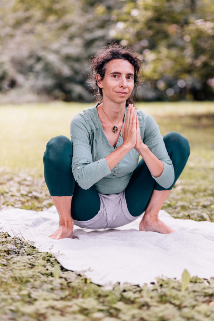 Die Yogalehrerin Maria Lichtenberg verweilt in einer tiefen Hocke und hält ihre Hände in Anjali mudra - die Füße sind gut verwurzelt, der Oberkörper aufgerichtet in der freien Natur (in der Nähe ihres Yogaraumes in Leipzig).