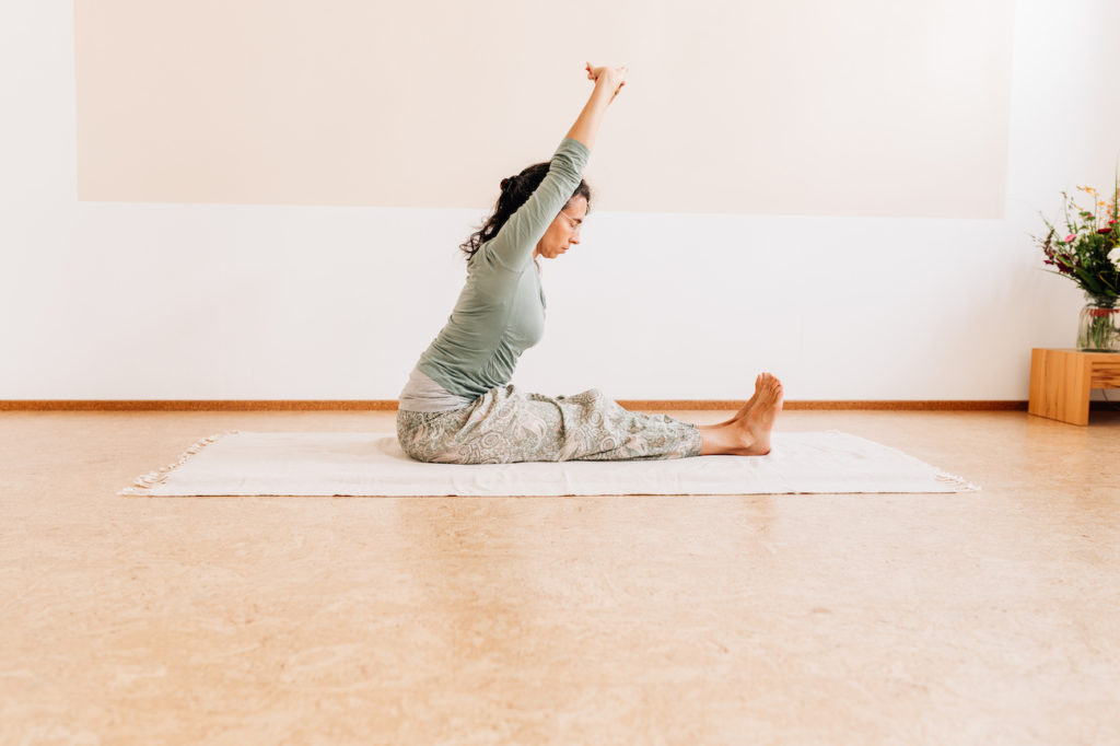 Die Yogalehrerin Maria Lichtenberg geht mit geradem Rücken und ausgestreckten Armen in eine klassische Vorbeuge im Sitzen in ihrem Yogaraum in Leipzig.