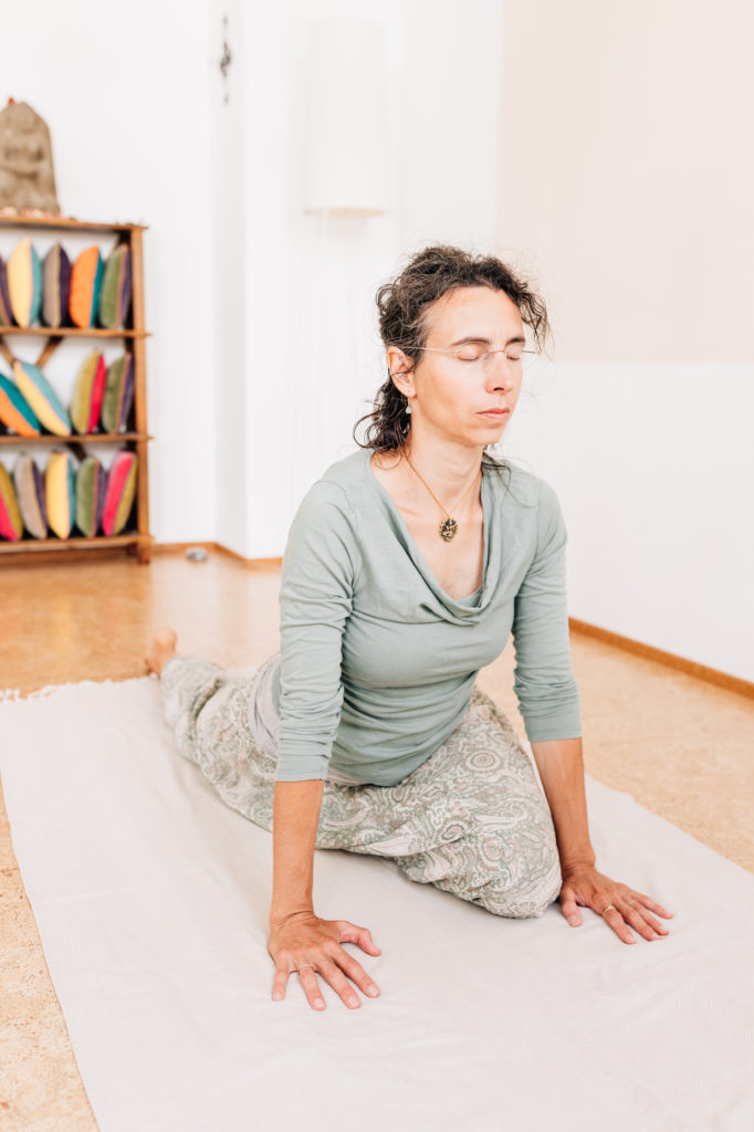 Die Yogalehrerin Maria Lichtenberg hat ein Bein nach hinten ausgestreckt während sie auf dem anderen angewinkelten Bein sitzt als Vorbereitung für die Haltung der Taube in ihrem Yogaraum in Leipzig.