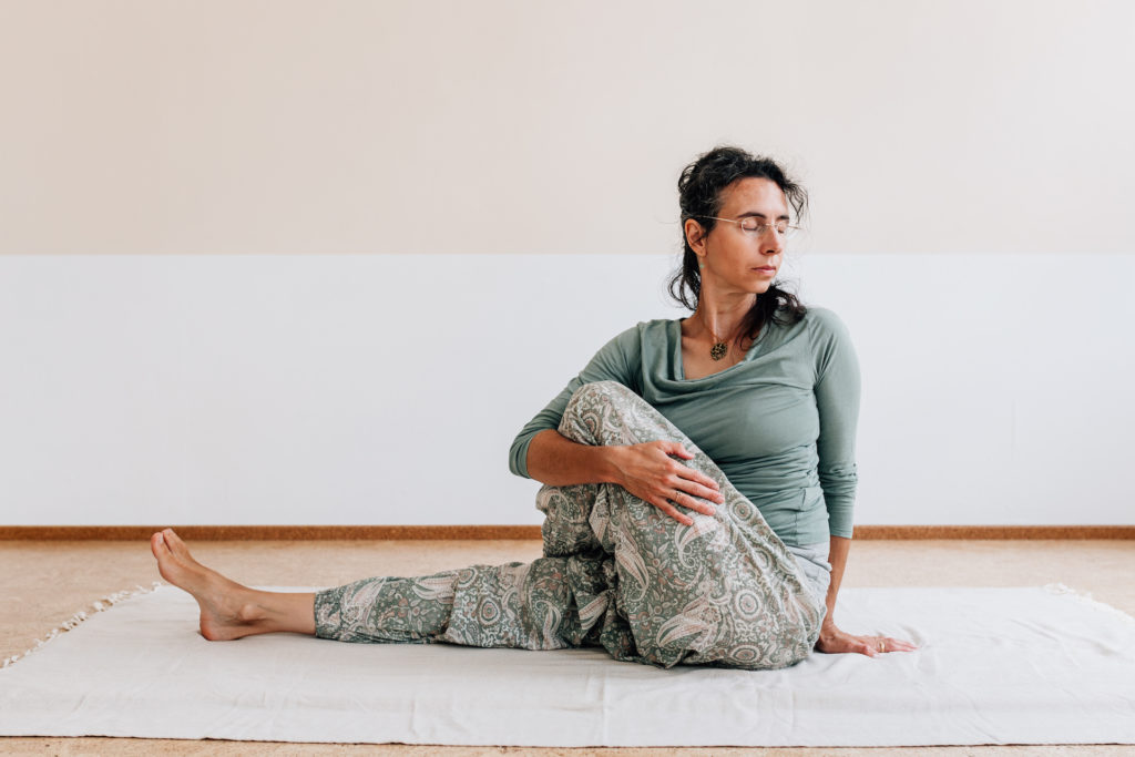 Die Yogalehrerin Maria Lichtenberg begibt sich mit einem ausgestreckten und einem angewinkelten Bein in den Drehsitz in ihrem Yogaraum in Leipzig.